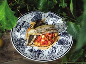 Caponata is spooned onto a heated plate, topped with fish and served with lemon halves.