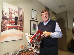 Former Canadiens general manager Serge Savard holds Hockey Hall of Fame Treasures book in his Montreal office in front of poster of him holding Stanley Cup with teammate Yvan Cournoyer during the Stanley Cup parade from the 1970s.