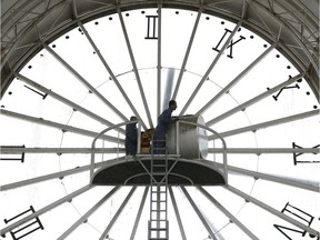 An employee climbs a ladder to check a huge clock in Cergy. France.