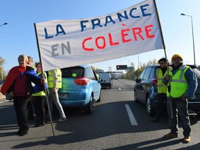 People holding a sign reading "France is angry" as they block the rocade (ring road) during a demonstration of the "yellow vest" (Gilets jaunes) movement against the rising of the fuel and oil prices on November 17, 2018 in Bordeaux, southwestern France.