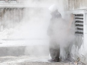 A Montrealer attempts to get warm from an exhaust vent during a cold snap in Montreal, on Thursday, January 2, 2014.