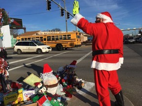 In this Dec. 18, 2018 photo, Jimmy Izbinski, wearing a Santa suit, waves to motorists passing the Christmas weed in Toledo, Ohio. The street corner weed decked out with lights and ornaments is spreading holiday goodwill.