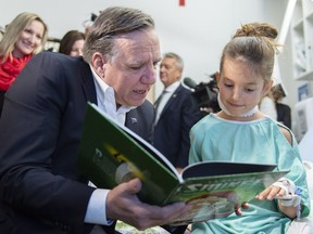 Quebec Premier François Legault reads a book with young Sara De Montigny during a visit at the St-Justine Hospital on Friday.
