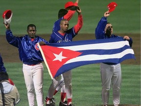 FILE - In this Monday, May 3, 1999 file photo, members of the Cuban baseball team carry their country's flag onto the field after a baseball game against the Baltimore Orioles at Camden Yards in Baltimore. Major League Baseball, its players' association and the Cuban Baseball Federation reached an agreement that will allow players from the island nation to sign big league contracts without defecting, an effort to eliminate the dangerous trafficking that had gone on for decades. The agreement runs through Oct. 31, 2021.