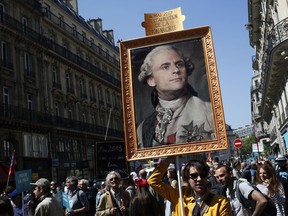 FILE - In this Saturday, May 5, 2018 file picture a protester carries a picture of French President Emmanuel Macron depicted as King Louis XVI during a protest in Paris. There are parallels for unpopular French President Emmanuel Macron in the demise of King Louis XVI more than two centuries ago. Democracy has replaced monarchy but the culture of a mob taking its anger against perceived inequality onto the streets of Paris has not changed.