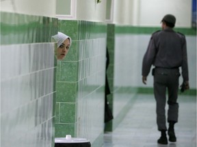 An inmate peers from behind a wall as a guard walks by at the female section of Evin jail in June 2006.