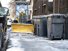 A snow-removal crew worker negotiates, with inches to spare, his way around garbage bins left on the sidewalk in Montreal, on Tuesday, Jan. 1, 2019. The driver was forced to leave his tractor and move some bins to be able to spread abrasives on the sidewalk.