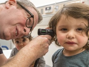 The MUHC's Dr. Harley Eisman checks out 2-year-old Emma-Rose Russo for the flu, as her 1-year-old sister, Zoe keeps a close eye on proceedings.