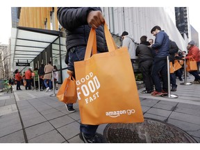 In this Monday, Jan. 22, 2018, file photo, a shopper walks past others in a line waiting to get inside an Amazon Go store in Seattle.