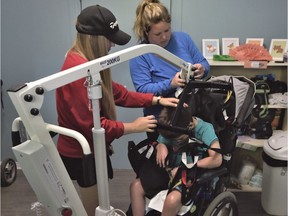 Mélissa Laprise and Sara-Émily Lauzon are installing Enzo Racine in the patient lift to move him to the bed for hygienic care in St-Lazare.