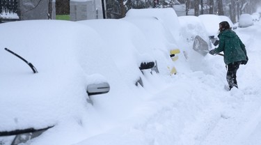 A woman digs her car out of a snowbank during a winter storm in Montreal on Wednesday, February 13, 2019. THE CANADIAN PRESS/Paul Chiasson ORG XMIT: pch108