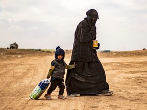 A fully veiled woman and a child approach a screening point for the hundreds of civilians who streamed out of the Islamic State group's last Syrian stronghold, outside Baghouz on March 5, 2019.