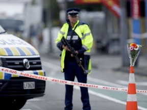 Flower rest at a road block, as a Police officer stands guard near the Linwood mosque, site of one of the mass shootings at two mosques in Christchurch, New Zealand, Saturday, March 16, 2019.