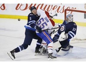 Winnipeg Jets goaltender Connor Hellebuyck saves the shot by Canadiens' Andrew Shaw (65) as Jets' Dmitry Kulikov (5) defends in Winnipeg on Saturday, March 28, 2019.