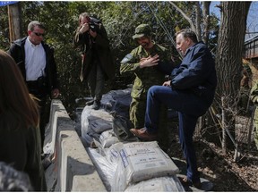 Premier François Legault gets help getting over a wall of sand made by the Canadian military on the Île-Bigras near Montreal on Sunday, April 21, 2019. Legault was touring areas of Laval affected by rising waters.