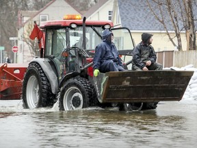 Richard Decoste, left, and Claude Gagnon ride in the bucket of a tractor on Filion St. in Lachute, west of Montreal Friday April 26, 2019.
