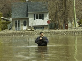 A photographer wades in the water on a flooded street in Ste-Marthe-sur-le-Lac near Montreal on Sunday, April 28, 2019, the day after Lac des Deux Montagnes breached a dike in the community. Several thousand people were forced from their homes  with little more than the clothes on their backs.