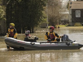 Firefighters move a man down a flooded street in Ste-Marthe-sur-le-Lac on Sunday April 28, 2019, the day after a dike was breached in the town.