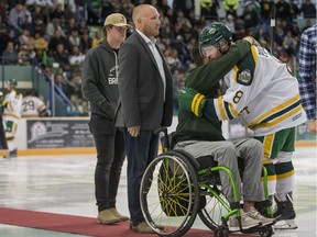 Humboldt Broncos'  forward Reagan Poncelet, right hugs bus crash survivor Jacob Wasserman as former Humboldt assistant coach Chris Beaudry looks on prior to the Broncos 2018 home opener game against the Nipawin Hawks in Humboldt on Sept. 12, 2018.