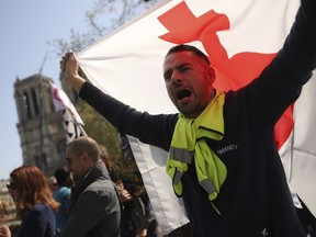 A man waves a flag near the Notre Dame Cathedral as he takes part in a yellow vest demonstration in Paris, Saturday, April 20, 2019. French yellow vest protesters are marching anew to remind the government that rebuilding the fire-ravaged Notre Dame Cathedral isn't the only problem the nation needs to solve.