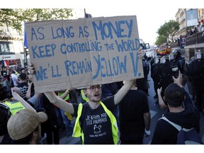 A man in a yellow vest holds up a sign at the Place de République during a yellow vest demonstration in Paris on Saturday, April 20, 2019.