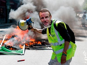 A protester wearing a mask of French President Emmanuel Macron crying stands next to a burning barricade during an anti-government demonstration called by the Yellow Vests (gilets jaunes) movement, on Saturday, April 20, 2019, in Paris.