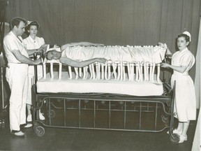 New frame bed for spinal cord patients at the Montreal Neurological Institute. Original cutline: "John Hogan of Massena, N.Y., victim of a motor accident, is turned every hour on the newly developed frame for patients with broken spinal cords at the Montreal Neurological Institute. Left to right are Dr. Gordon Dugger, Miss Mary Cavanagh and Miss Mary Morrison."