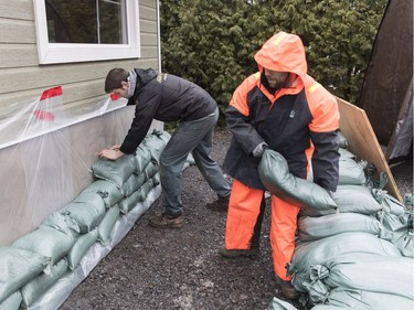 Two men place sandbags next to the foundation of a house in Rigaud, on Friday, April 19, 2019.