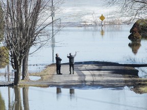 Two men look out toward the Ottawa River on a residential street surrounded by floodwaters in Rigaud, Monday, April 22, 2019.