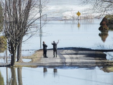 Two men look out towards the Ottawa River on a residential street surrounded by floodwaters in the town of Rigaud, Monday, April 22, 2019.