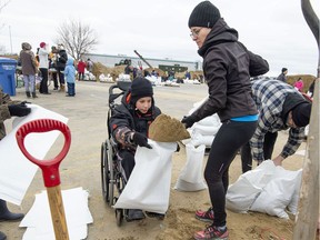 Ten-year-old Xavier Poitras, who has cerebral palsy, helps his mother Caroline Bouchard, right and brother Benjamin, left, fill sandbags in Vaudreuil-Dorion, Que., on Sunday, April 28, 2019