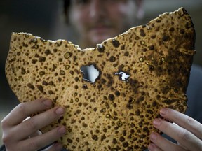 FILE - In this Wednesday, April 13, 2016 photo, an Orthodox Jewish man holds a piece of matzo, or unleavened bread. Its uneven shapes shows that it has been handmade and not commercially prepared. Photo was taken at a Hasidic  community bakery in Netanya, Israel. Jews who observe the eight-day Jewish holiday of Passover do not eat leavened foods, including bread, Passover celebrates the biblical story of the liberation of the Israelites from slavery in Egypt.
