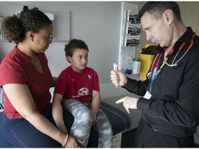 Dr. Moshe Ben-Shoshan explains the workings of an EpiPen to Yohan-Thomas Sénéchal, sittng with his mother, Yolaine Paul, at the Montreal Children's Hospital on Thursday.