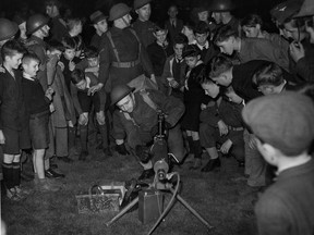 An excerpt from the original caption, dated May 9, 1942: "Men of the Royal Montreal Regiment (M.G.) had an eager audience of youngsters, as well as grown-ups, during a realistic military outdoor display which was given last night before a large crowd in Montreal West park, at Westminster Ave. and Broughton Road. Lieut. Lorne Gales is seen above manipulating a Vickers machine gun while his youthful audience watches intently."