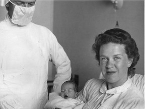 Montreal General Hospital president W.S.M. MacTier had to don a sterile gown and mask to present a silver christening mug to Una Patricia Dobell, the first baby born in the Cedar Avenue building of the Montreal General. The mug was received by the baby's mother, Mrs. Alfred M. (Elizabeth) Dobell. This photo was published in the Montreal Gazette on May 31, 1955.