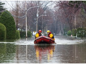 Firefighters make their way through a flooded street on Friday, May 3, 2019 in Ste-Marthe-sur-la-Lac, Que.