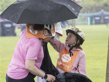Seven year-old Floralie Binet brings up umbrella to help her mother Ophélie Rivière change into some sturdier rain gear as they take part in the Tour de l'Ile in René-Lévesque Park in Lachine on Sunday June 2, 2019.