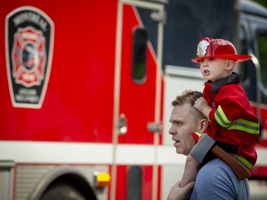 MONTREAL, QUE.: JUNE 29, 2019 --  3-year-old Bernard Dionne sits on his fathers shoulders as he watches a long line of firetrucks parade past them on Mount Royal Ave in Montreal, on Saturday, June 29, 2019. The parade is part of the 75 year anniversary of the The Montreal Auxiliary Firemen in Montreal.  (Peter McCabe / MONTREAL GAZETTE) ORG XMIT: 62782