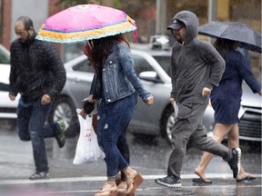 People huddle under umbrellas or run to cross the street during a downpour in Montreal June 25, 2019.