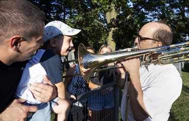 MONTREAL, QUE.: July 23, 2019 -- OSM trombonist Pierre Beaudry plays for 3-year-old Matteao Russo before the OSM performs in Wilfrid-Bastien Park as part of the Conseil des arts de Montreal OSM in the Parks series, in Montreal, on Tuesday, July 23, 2019. Matteo's father, Michael Anthony Russo holds Matteo as sits on a fence to be able to interact with Beaudry. (Allen McInnis / MONTREAL GAZETTE) ORG XMIT: 62893