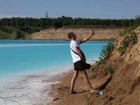 A man takes a selfie picture by a Novosibirsk energy plant's ash dump site - nicknamed the local "Maldives" - on July 11, 2019. - An industrial dump site in Siberia whose turquoise lake resembles a tropical paradise has become a magnet for Instagrammers who risk their health in the toxic water to wow online followers.