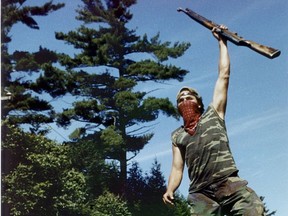 A Mohawk Warrior stands atop a just-made barricade in Oka on July 11, 1990 at the start of the Oka crisis. (The uncropped vertical photo is inset into the text.)