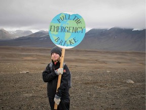 TOPSHOT - An Icelandic girl poses for a photo with a "Pull the emergency brake" sign near to where a monument was unveiled at the site of Okjokull, Iceland's first glacier lost to climate change in the west of Iceland on August 18, 2019.