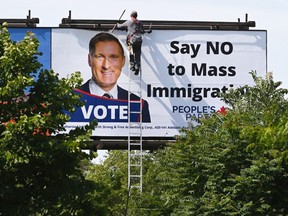 A worker removes a billboard featuring the portrait of People's Party of Canada (PPC) leader Maxime Bernier and its message "Say NO to Mass Immigration" in Toronto on Monday, Aug. 26, 2019.