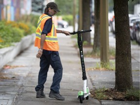 A city worker moves a Lime Scooter that was left in the middle of the side walk along Saint-Antoine Street in Montreal, on Wednesday, August 21, 2019.