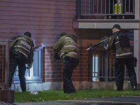 Heavily armed Sûreté du Québec officers break the window to a basement apartment where a man was reported to be hiding in St-Lazare, west of Montreal, on Sunday, Oct. 27, 2019.