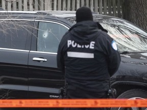 A Montreal police officer stands next to SUV with bullet hole in its window in St-Leonard in 2018.