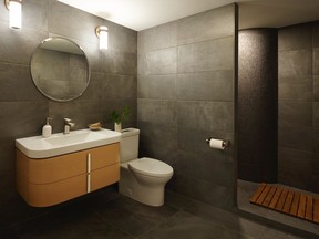 Dark tiled walls and floors create a modern, moody en-suite bathroom. Natural oak vanity, brushed nickel faucet and Canvas white toilet and sink, part of the Equility Collection, DXV.com
