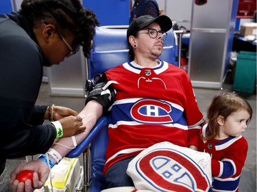 Three-year-old Zoe Garcaeu and her father, Mathieu Garceau, look away as a nurse pokes him with a needle during the annual Montreal Canadiens' blood drive at the Bell Centre on Wednesday, Oct. 23, 2019.