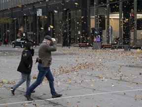 Montrealers brave high winds and blowing leaves as they cross Rene-Levesque near Peel Nov. 1, 2019.